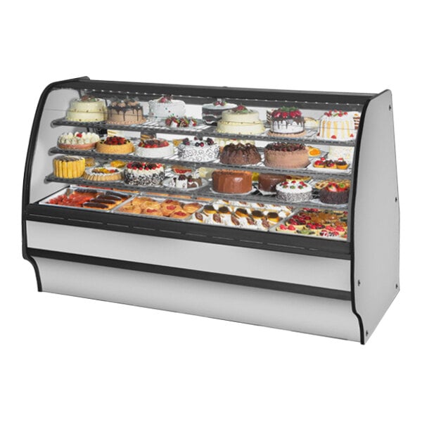 A True refrigerated bakery display case with a curved glass front filled with cakes.