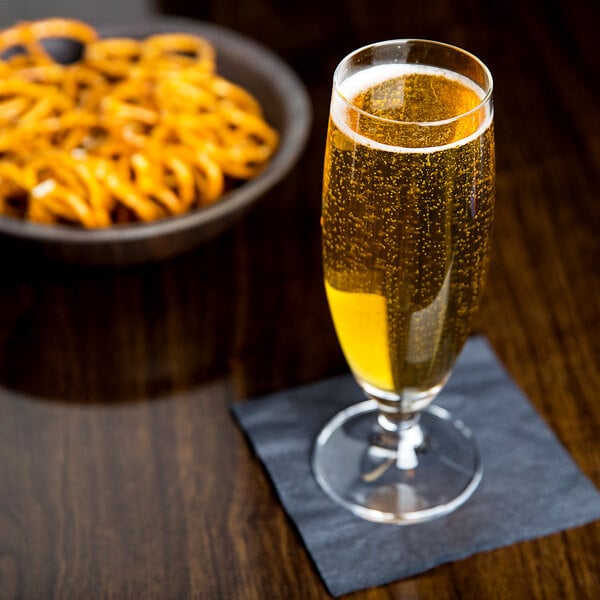 A Stolzle stemmed beer glass filled with beer next to a bowl of pretzels.