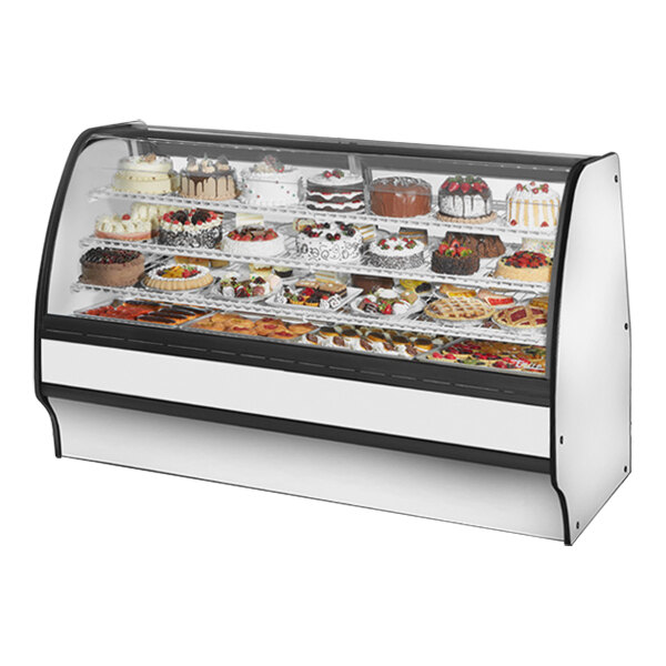 A True refrigerated bakery display case with a white interior and curved glass filled with cakes.