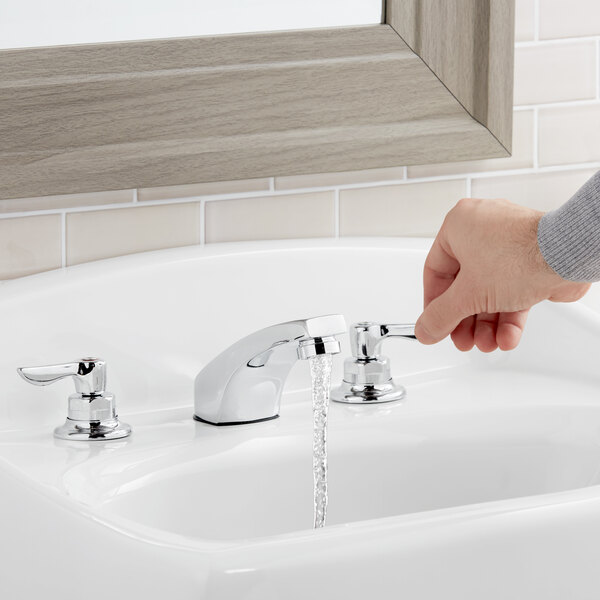 A hand pressing the American Standard Monterrey deck-mount faucet on a counter.