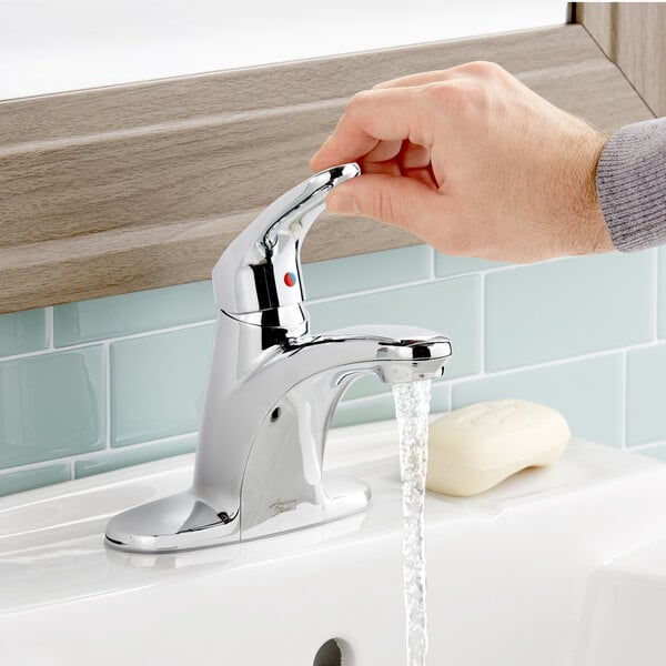 A hand holding the American Standard Colony Pro single lever faucet with water running.