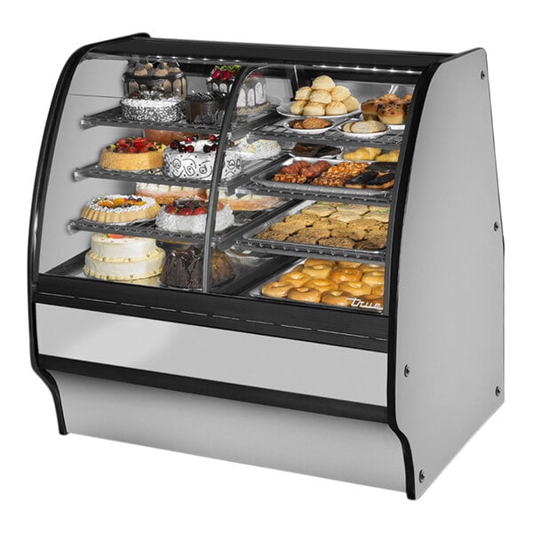 A True dual zone refrigerated bakery display case with a curved glass front filled with cakes and pastries.