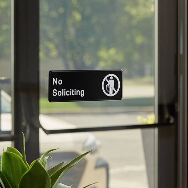 A Lavex No Soliciting sign with black text on a white background on a glass door in a restaurant.