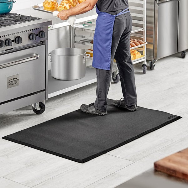 A man standing on a Lavex heavy-duty black anti-fatigue floor mat in a kitchen.