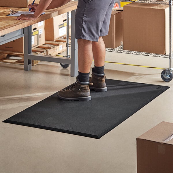 A person standing on a Choice black anti-fatigue floor mat at a table.