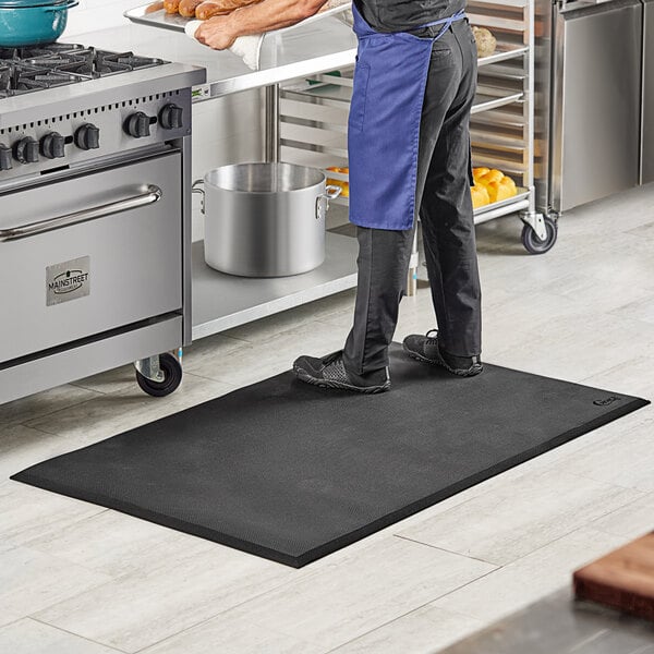 A man standing on a black Choice anti-fatigue floor mat in a kitchen.