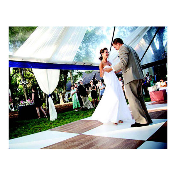 A man in a suit dancing with a woman in a white dress on a white checker portable dance floor.