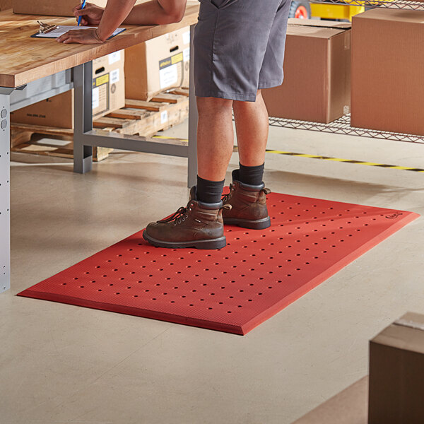 A man standing on a red Choice anti-fatigue floor mat with drainage holes.