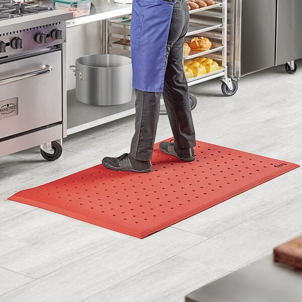 A person standing on a red Choice anti-fatigue floor mat in a kitchen.