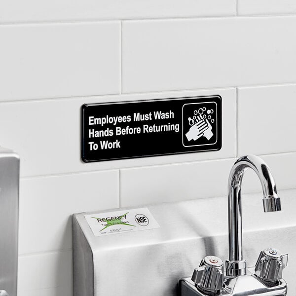 A black and white Lavex Employees Must Wash Hands Before Returning to Work sign on a wall.