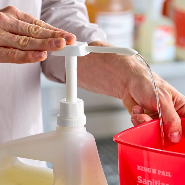 A white plastic syrup or condiment pump dispensing liquid into a red container.