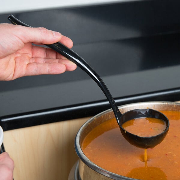 A person using a black Sabert ladle to pour soup into a bowl.