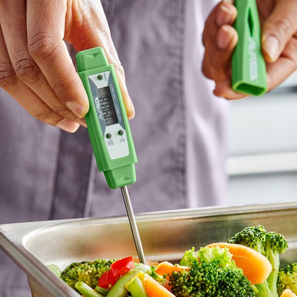 A green digital pocket probe thermometer being used to measure the temperature of cooked vegetables.