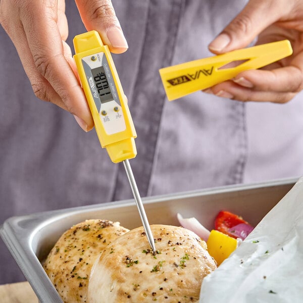 A yellow digital pocket probe thermometer being used to check the temperature of cooked chicken.