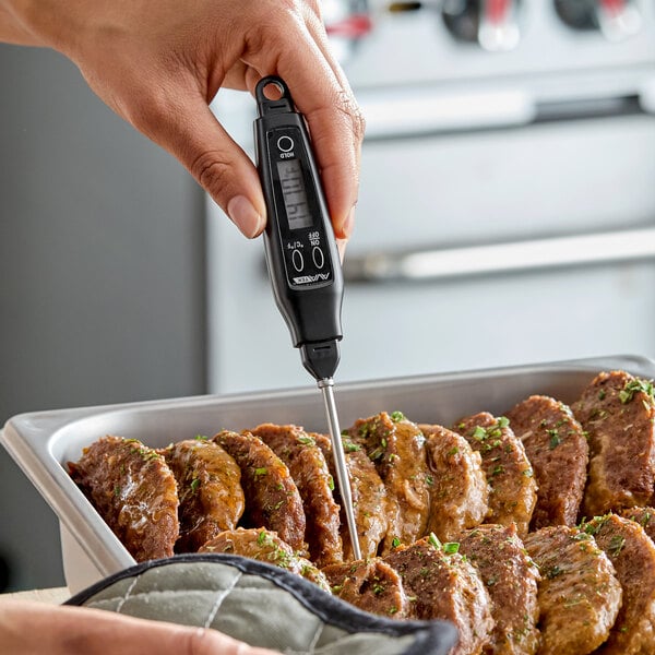 A black digital pocket probe thermometer being used to check the temperature of cooked meat in a tray.