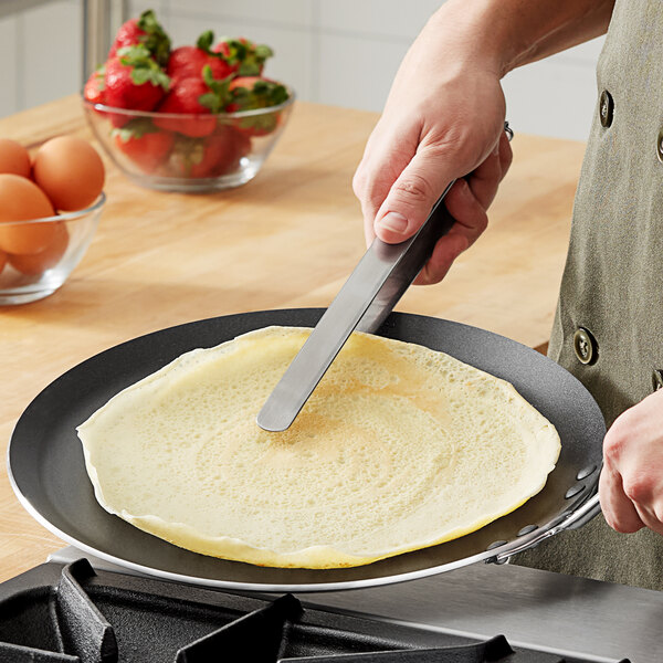 A person using Choice stainless steel tongs to serve a pancake.