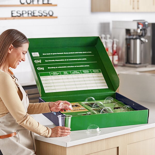 A woman putting a plastic cup into a green box on a counter.