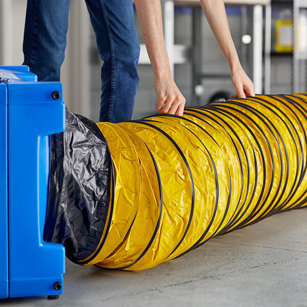 A person using a Lavex flexible yellow tube to connect to a blue air scrubber.