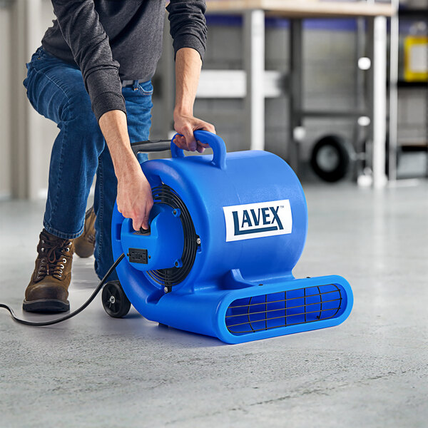 A woman using a Lavex blue air mover with telescoping handle and wheels to clean a floor.