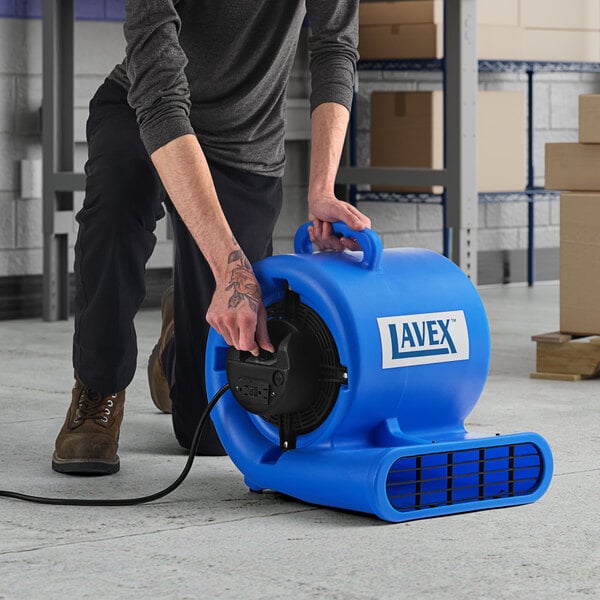 A man using a blue and black Lavex 3-speed commercial air mover to clean a floor.