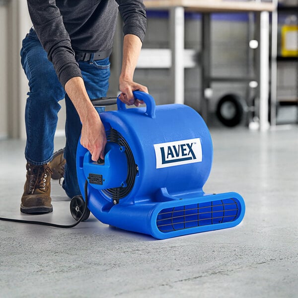 A man using a blue Lavex air mover with wheels and a telescoping handle.