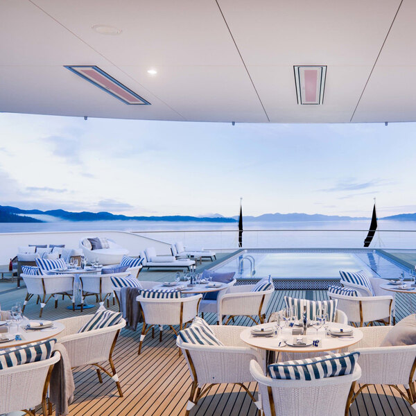 A white Bromic Heating marine patio heater above a table and chairs on a deck overlooking water.