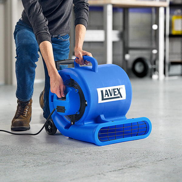 A man using a blue Lavex air mover with telescoping handle and wheels to clean a floor.