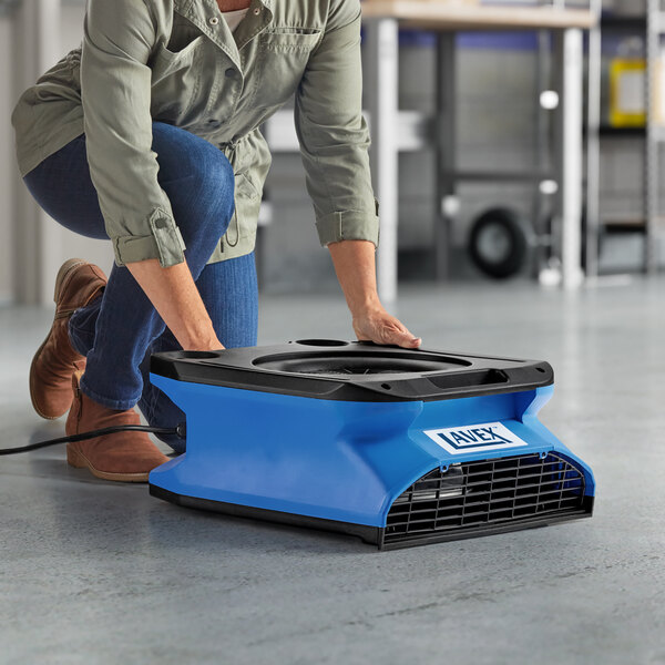 A woman using a blue and black Lavex air blower on the floor.