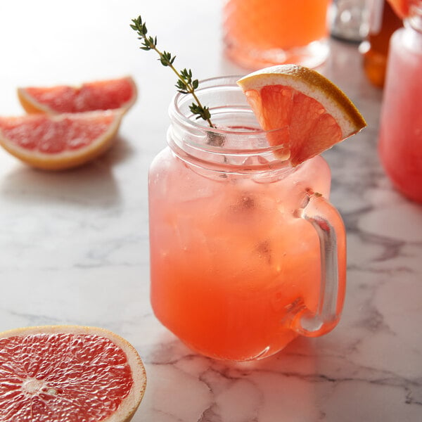 A glass of grapefruit juice with a slice of grapefruit on the rim using Monin Premium Ruby Red Grapefruit Flavoring Syrup.