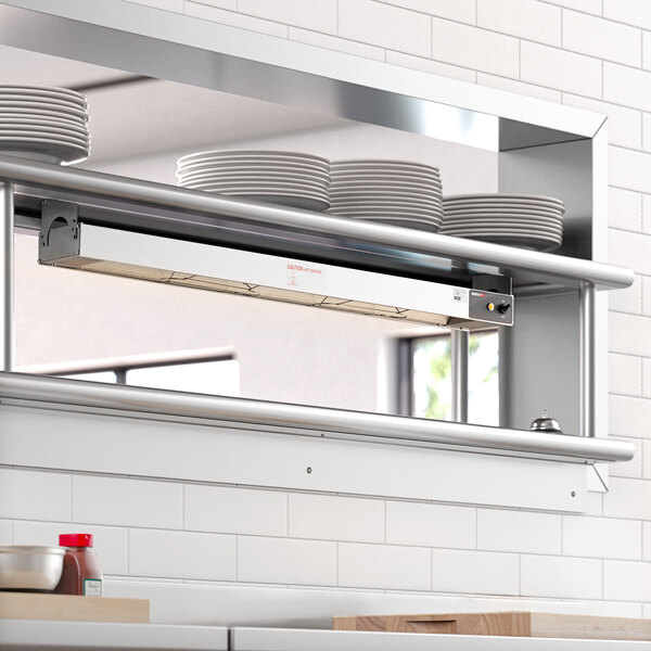 A ServIt strip warmer on a shelf above plates in a professional kitchen.