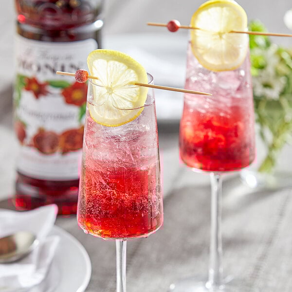 A close-up of two glasses of red liquid with lemon slices and straws on a table.
