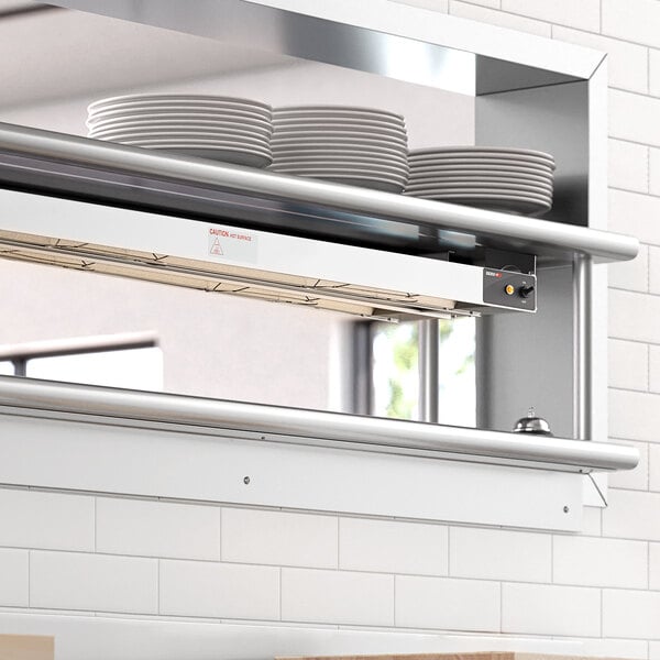 A ServIt double strip warmer on a shelf above plates in a professional kitchen.