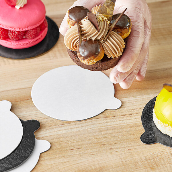 A hand holding a chocolate covered pastry on a white and black Enjay dessert board.