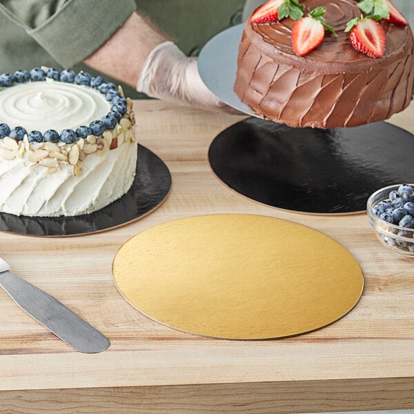 A person setting a white frosted cake on a gold and black Enjay dessert board on a table.