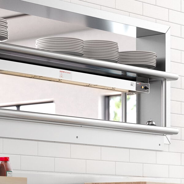 A stainless steel shelf with a ServIt Strip Warmer above plates on a counter in a professional kitchen.