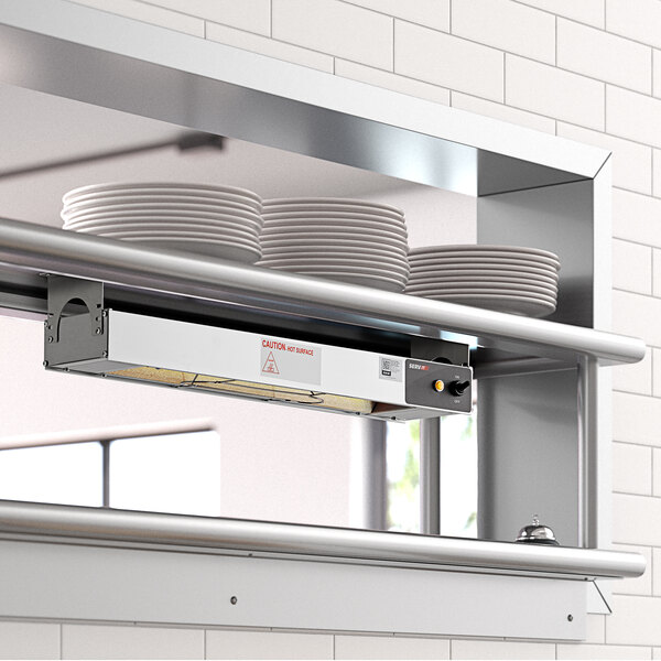 A ServIt strip warmer mounted on a wall above a counter in a school kitchen.