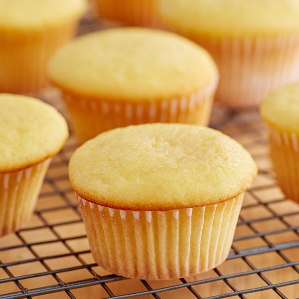 White fluted baking cups filled with yellow cupcakes on a wire rack.