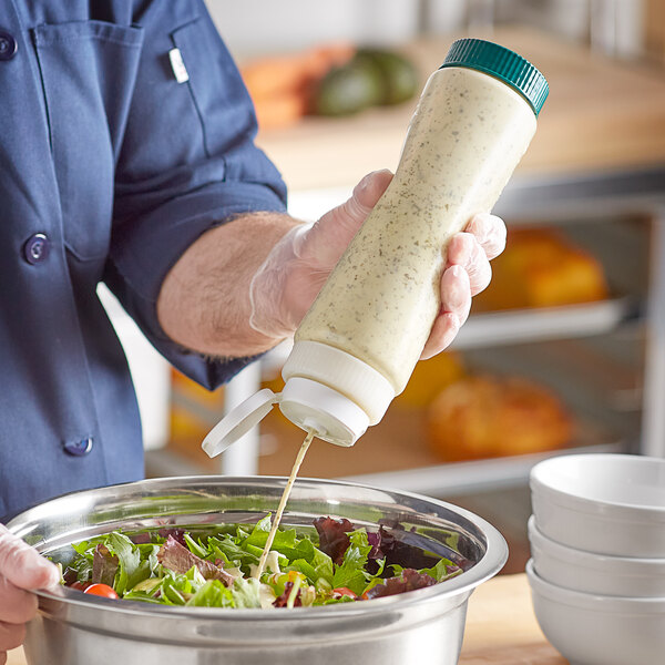 A person using a Vollrath Traex clear squeeze dispenser to pour dressing onto a bowl of salad.