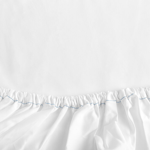 A close-up of a white Garnier-Thiebaut fitted sheet with blue border and blue thread.