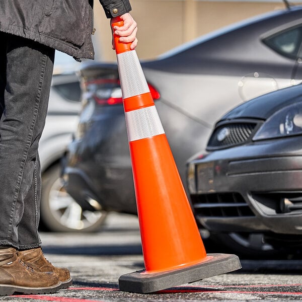 A person holding an Xpose Safety orange traffic cone with double reflective collars.