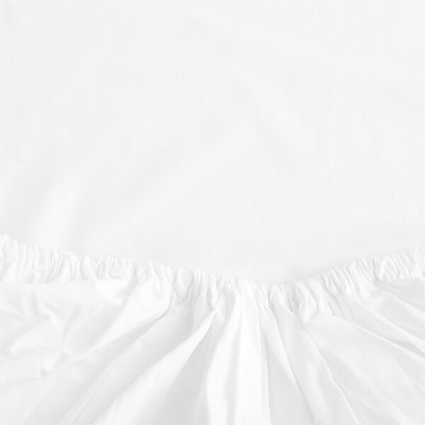 A close-up of a white Garnier-Thiebaut fitted sheet with ruffled fabric on the edges.