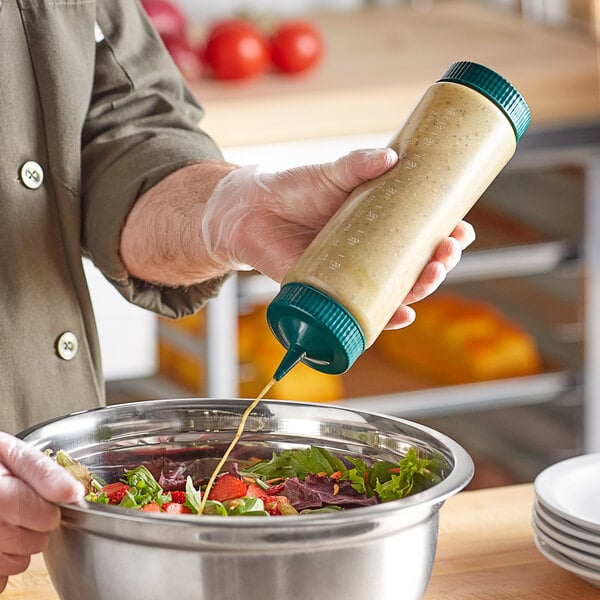 A person using a Vollrath Traex clear squeeze bottle to pour dressing on a bowl of salad.