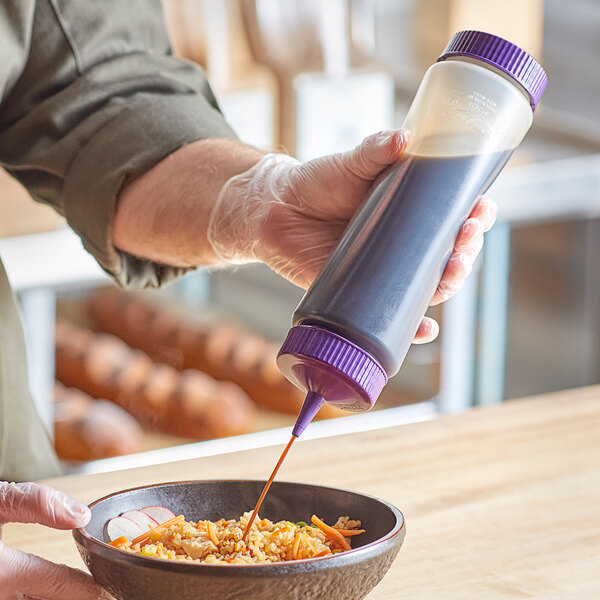 A hand pouring purple sauce from a Vollrath Traex squeeze bottle into a bowl of food.