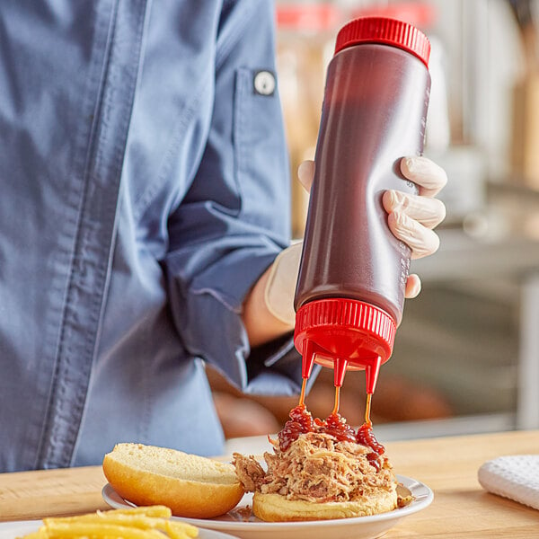 A hand using a Vollrath Traex squeeze bottle to pour sauce onto a sandwich.