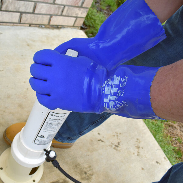A pair of blue Cordova Flex-Rite PVC gloves being worn by a person working with outdoor equipment.