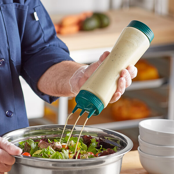 A person pouring dressing into a white bowl from a Vollrath Traex squeeze bottle.