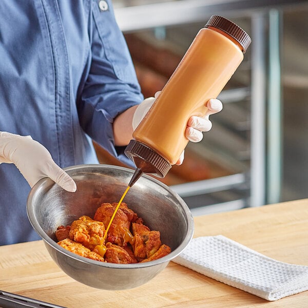 A person using a Vollrath Traex squeeze bottle to pour liquid into a bowl of food.