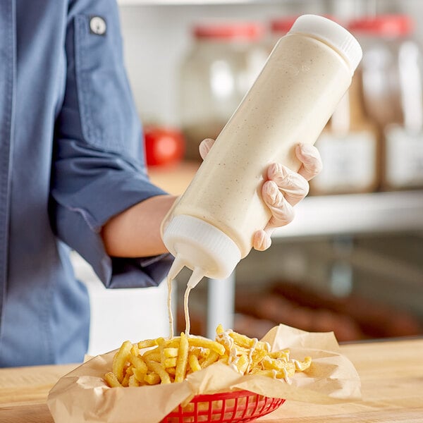 A person using a Vollrath Traex squeeze bottle to pour mayo onto a basket of french fries.