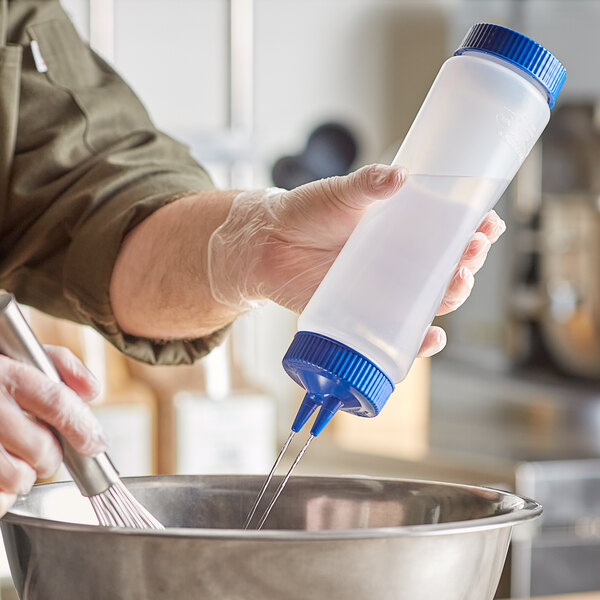 A person pouring liquid from a Vollrath Traex clear plastic squeeze bottle into a metal bowl.