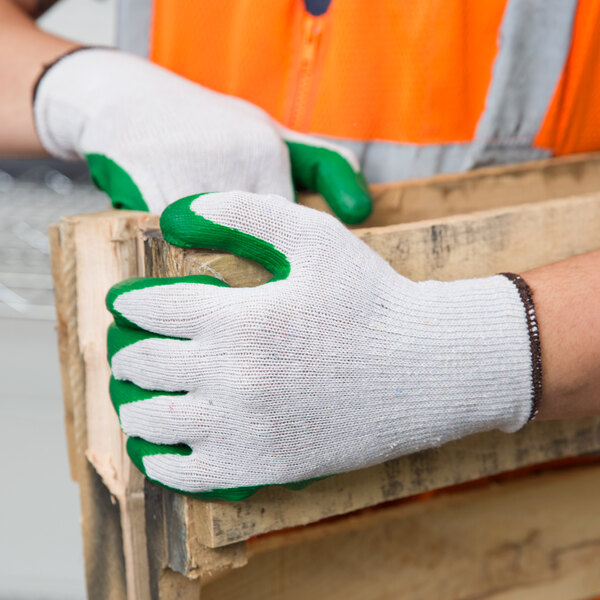 A person wearing Cordova warehouse gloves with green latex palm coating holding a piece of wood.